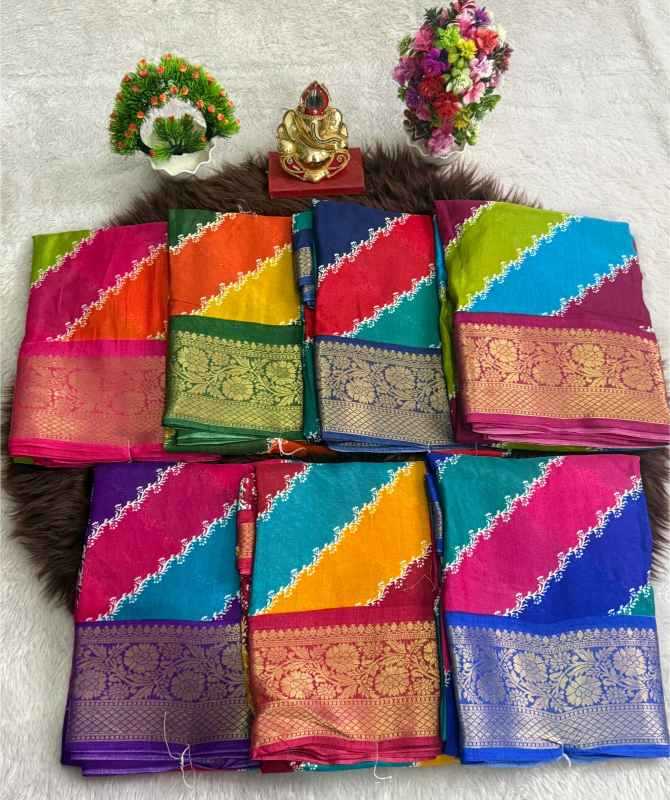 Eight folded colorful sarees with ornate gold zari borders are arranged in two rows on a dark brown faux-fur rug. The background is a white textured fabric, decorated with small floral and decorative props at the top.