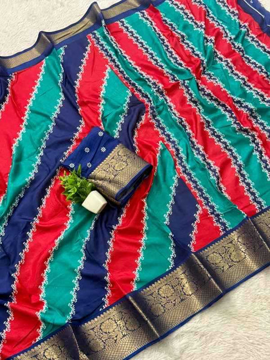 A multicolor striped saree fabric with diagonal bands of red, teal green, and navy blue, decorated with white embroidered borders and a wide gold zari metallic border. A matching navy blue and gold embroidered fabric piece is folded and styled with a small green plant sprig on a white textured background.
