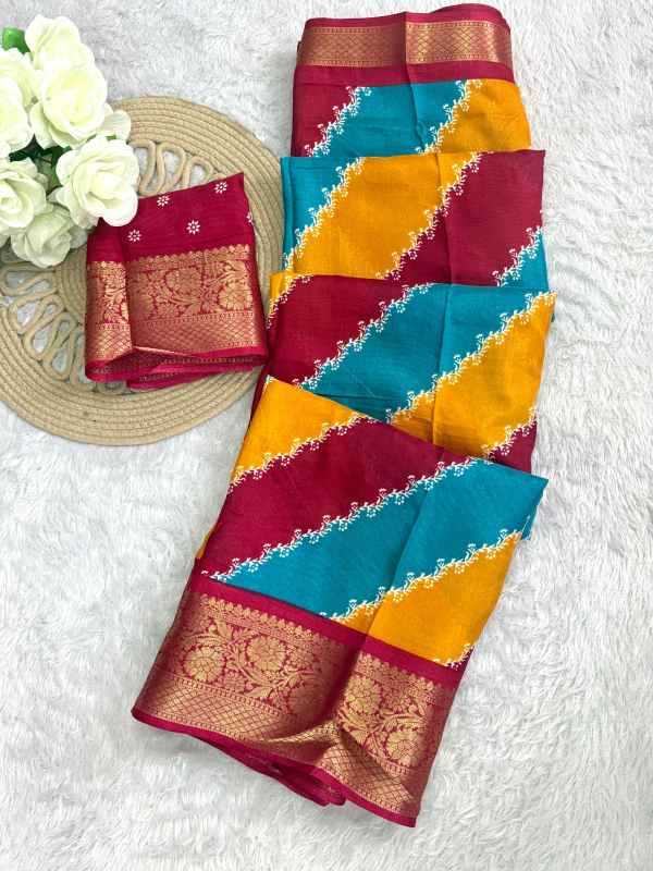 A folded multicolor saree with diagonal stripes of teal blue, mustard yellow, and deep red, featuring ornate gold zari borders and a wide red pallu, displayed on a white textured background next to white roses and a woven mat.