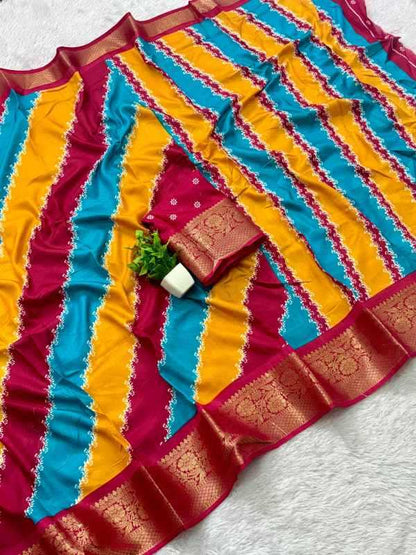 A multicolor striped saree or fabric piece with vertical bands of yellow, turquoise blue, and deep magenta, featuring ornate gold zari borders and a matching folded fabric accessory with a small green leaf accent, laid flat on a white textured surface.