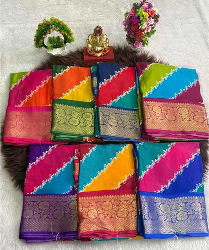 Eight folded colorful sarees with ornate gold zari borders are arranged in two rows on a dark brown faux-fur rug. The background is a white textured fabric, decorated with small floral and decorative props at the top.