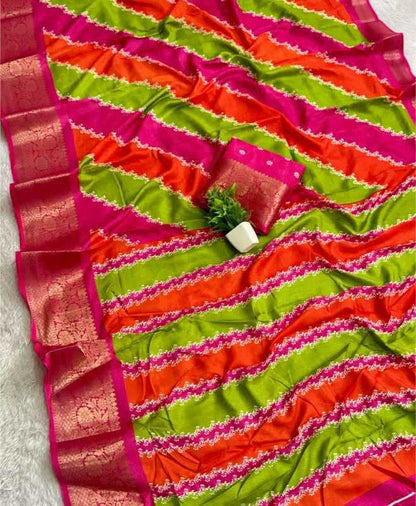 A vibrant striped saree with diagonal bands of lime green, orange, and magenta pink, featuring a wide metallic gold border and a matching small fabric blouse piece.