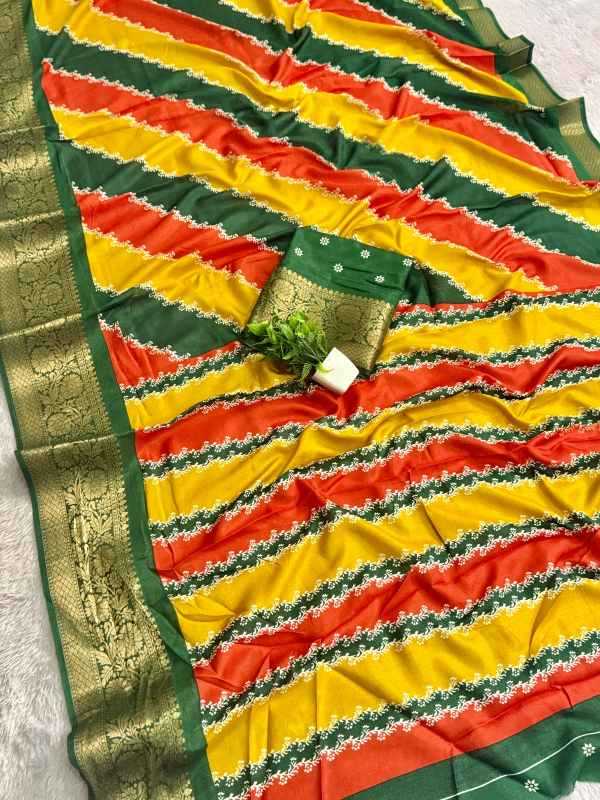 A striped saree fabric with diagonal bands of yellow, orange-red, and dark green, featuring a wide gold-patterned border and a matching green fabric piece with a small decorative plant and white tag placed on top.