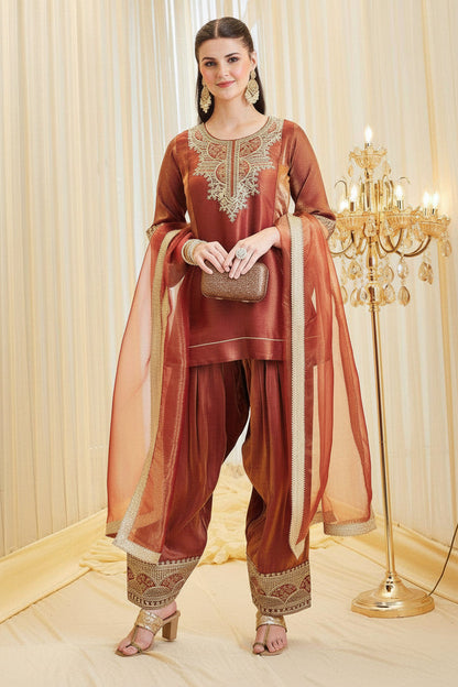 Woman in traditional maroon outfit with gold embroidery in a decorated room.