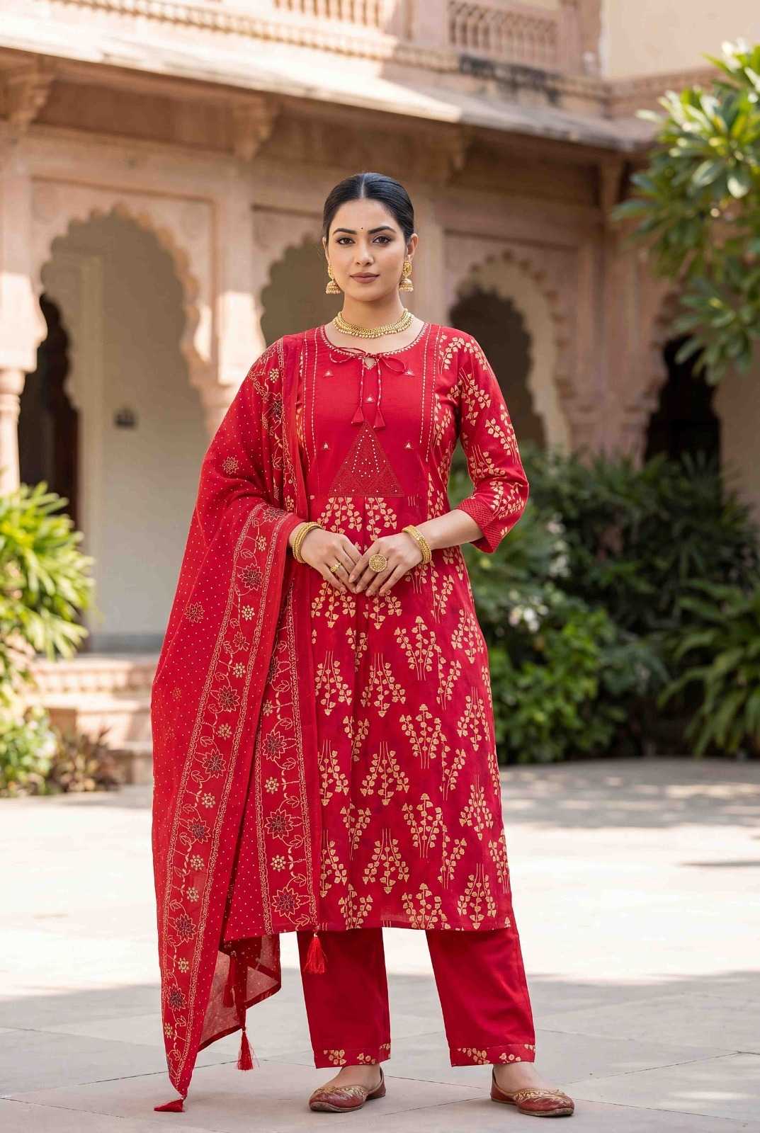 Woman wearing a red traditional outfit with floral patterns in an outdoor setting.