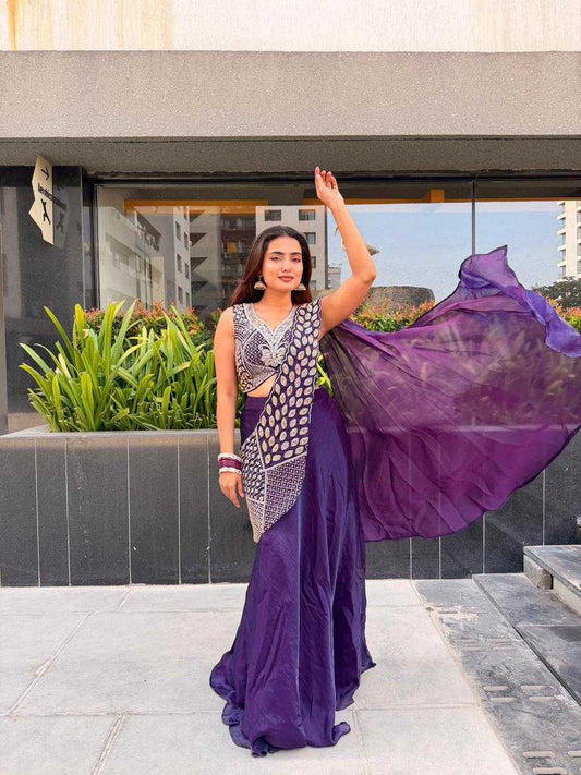 Woman in a purple saree with a patterned blouse standing outdoors.