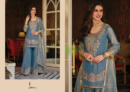 Woman in a blue embroidered traditional outfit standing in a decorated room.