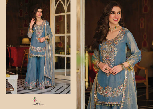 Woman in a blue embroidered traditional outfit standing in a decorated room.