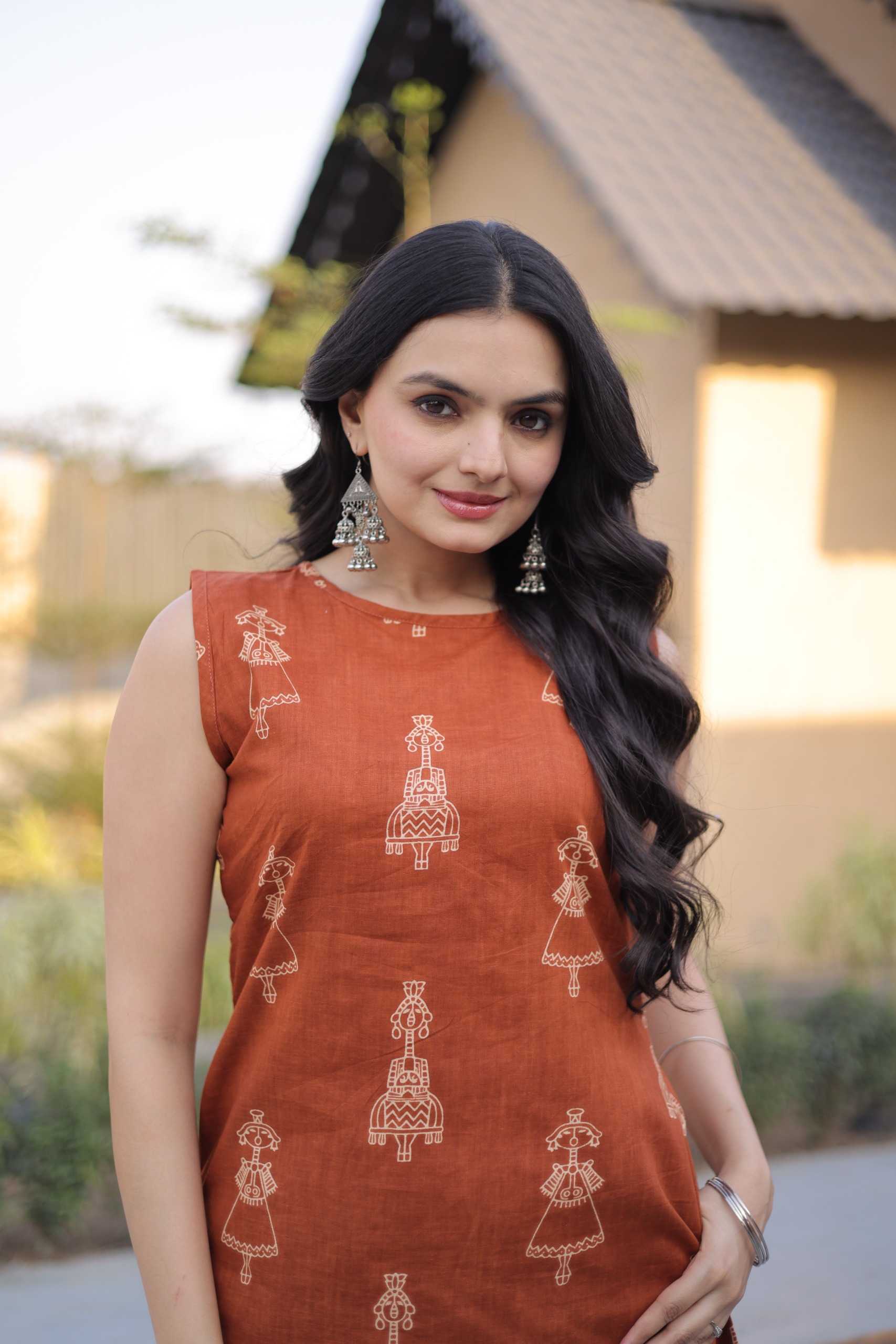 Woman wearing an orange traditional outfit with intricate patterns outdoors.