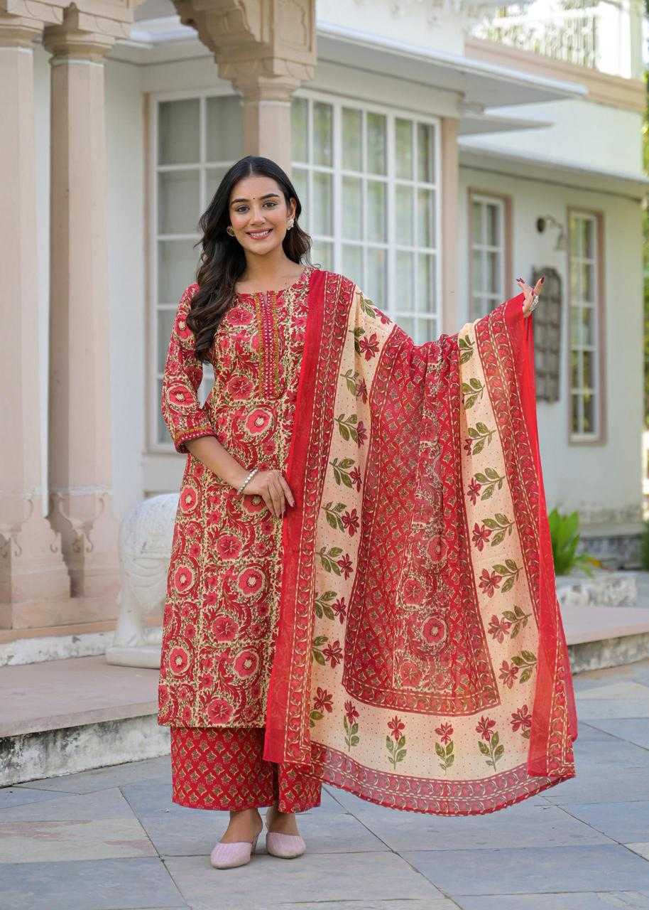 Woman in a red and beige traditional outfit standing outside a building.