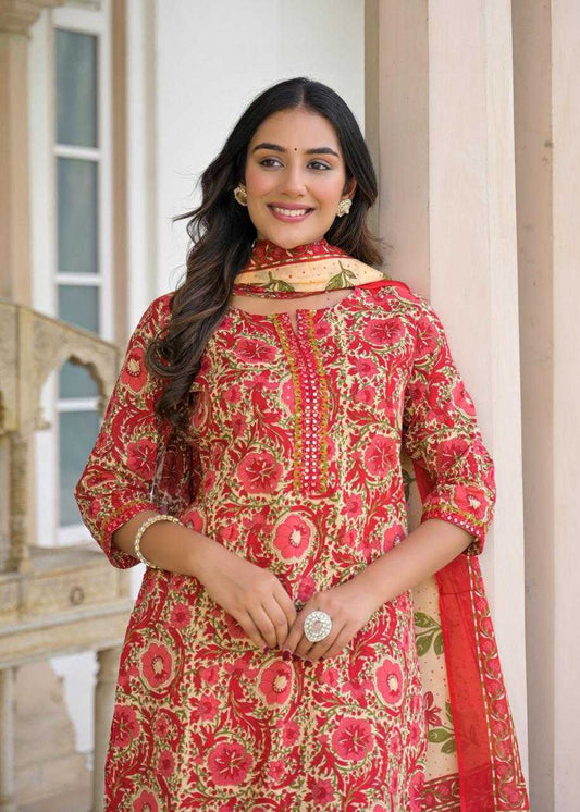 Woman wearing a red floral traditional outfit with a beige dupatta in an outdoor setting.
