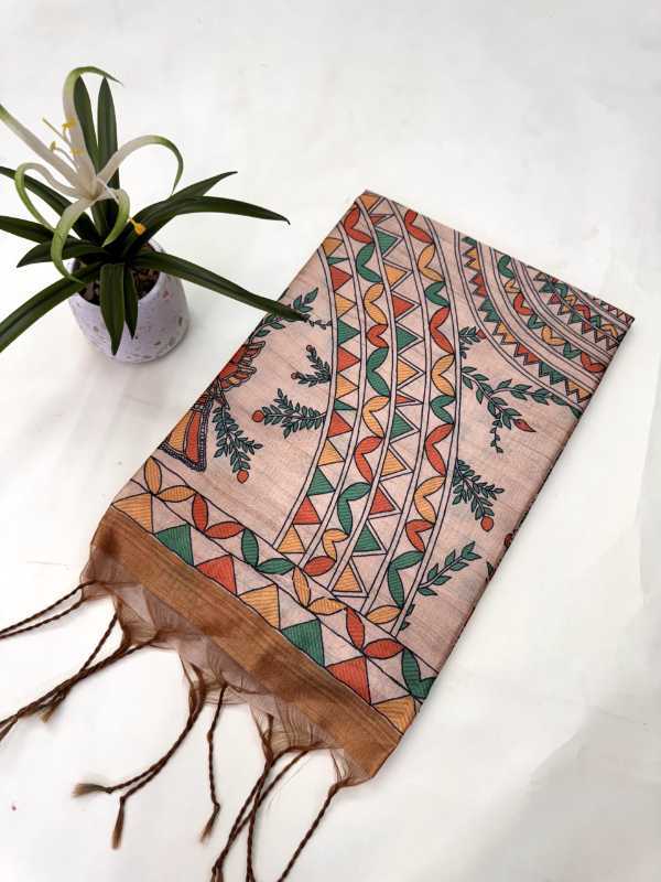 A rectangular scarf with fringed tassels, featuring a geometric tribal pattern in orange, green, and brown on a light beige background, styled on a white surface next to a small potted plant.