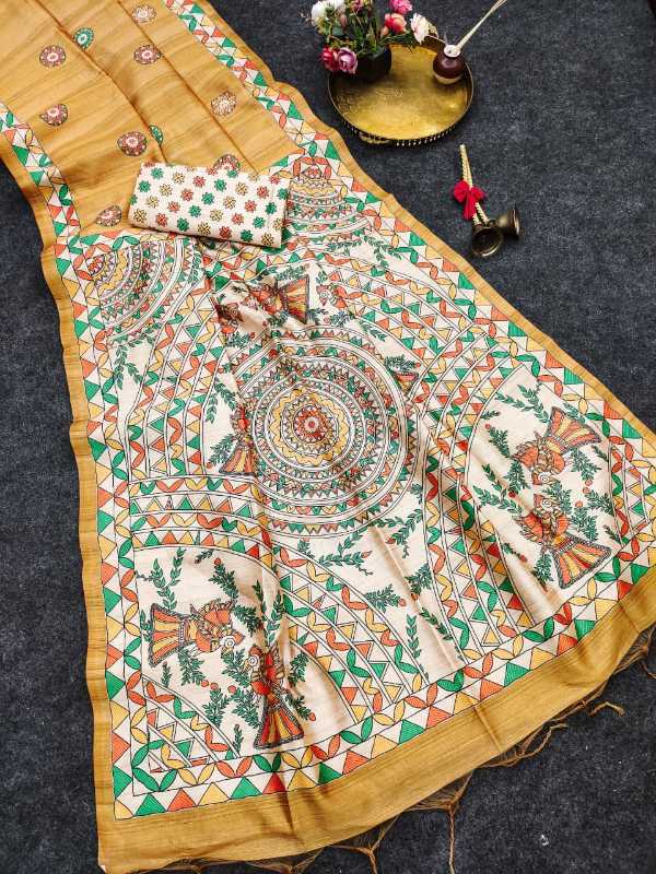 A mustard yellow and cream cotton saree with intricate hand-painted mandalas, floral motifs, and traditional geometric borders, styled on a dark gray textured background with decorative props.