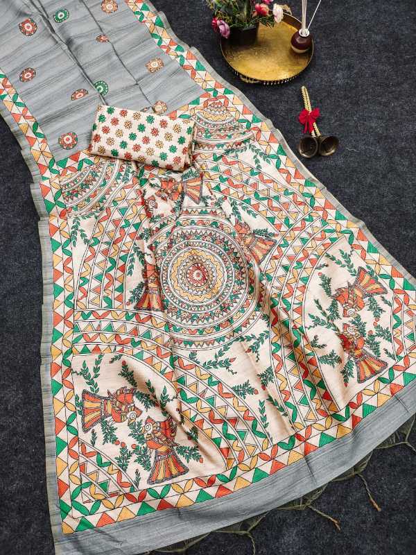 A printed cotton saree or fabric set laid flat on a dark textured surface, featuring a light gray base with a large cream panel decorated with colorful mandala and floral motifs in green, orange, red, and yellow. A matching patterned fabric piece and a small decorative tray with flowers are placed nearby.