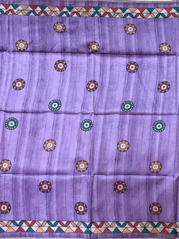 A lavender purple fabric, likely a saree, featuring a subtle vertical texture and a repeating pattern of circular floral motifs in brown, green, and white. The fabric is finished with decorative borders at the top and bottom containing a geometric triangle pattern in green, orange, and white.