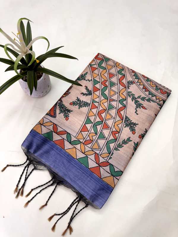 A folded patterned scarf with black tassels, featuring a beige base with colorful geometric and botanical motifs, and a solid blue border, displayed next to a small potted plant on a white background.