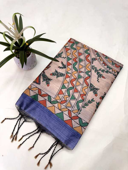 A folded patterned scarf with black tassels, featuring a beige base with colorful geometric and botanical motifs, and a solid blue border, displayed next to a small potted plant on a white background.