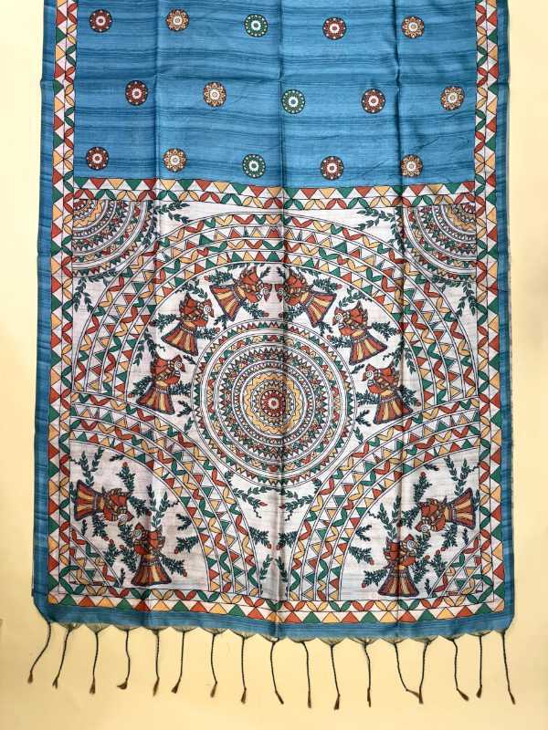 A blue and white patterned fabric, likely a sari or scarf, featuring intricate hand-painted style motifs, geometric borders, and a tassel fringe at the bottom, displayed flat against a light beige background.
