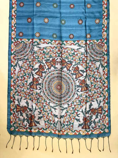 A blue and white patterned fabric, likely a sari or scarf, featuring intricate hand-painted style motifs, geometric borders, and a tassel fringe at the bottom, displayed flat against a light beige background.