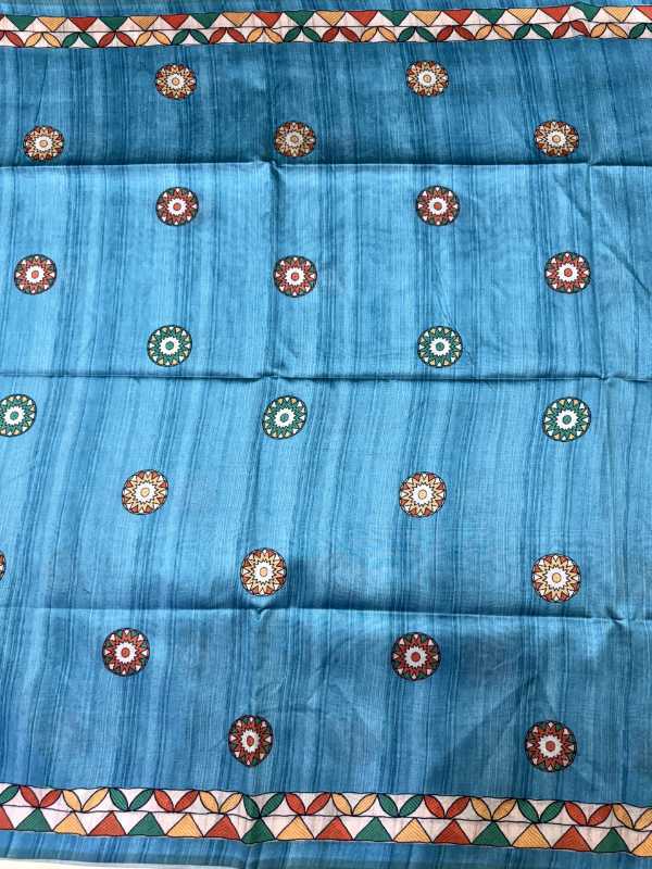 A blue fabric panel or scarf featuring a vertical textured stripe pattern and repeated circular floral motifs in red, green, and cream, with geometric borders at the top and bottom.