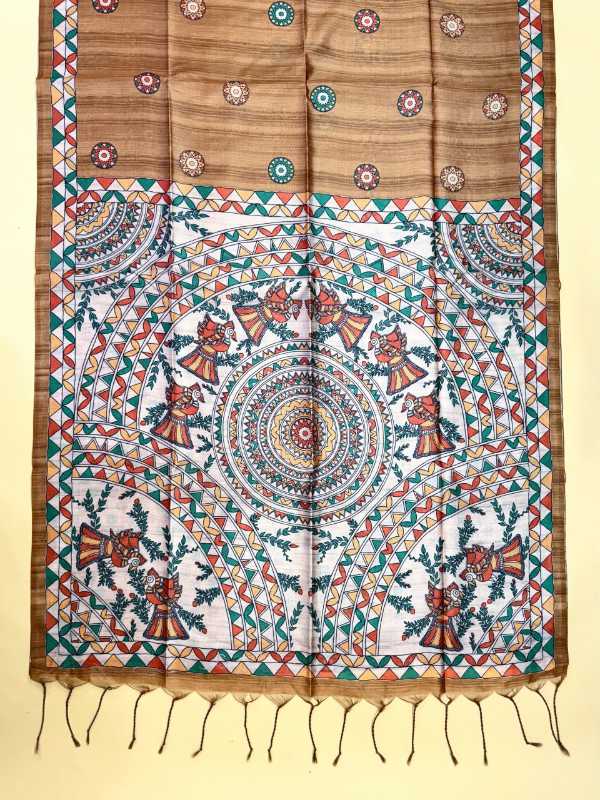 A traditional Indian cotton saree displayed flat against a light beige background. The saree features a warm brown upper section with small floral motifs, a white lower section with a large central mandala, and a colorful border with geometric patterns in red, green, and blue, finished with a fringed hem.