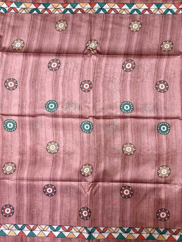 A dusty rose pink fabric, likely a saree, featuring a subtle vertical stripe texture and decorated with small circular mandala motifs in green, gold, and white. The fabric is finished with a colorful geometric border pattern at the top and bottom.