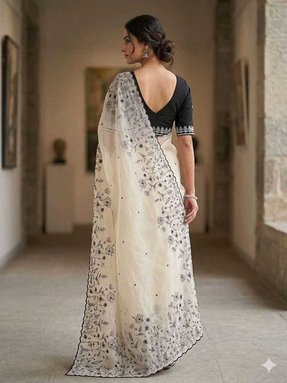Woman wearing a white saree with black floral patterns in an indoor setting.
