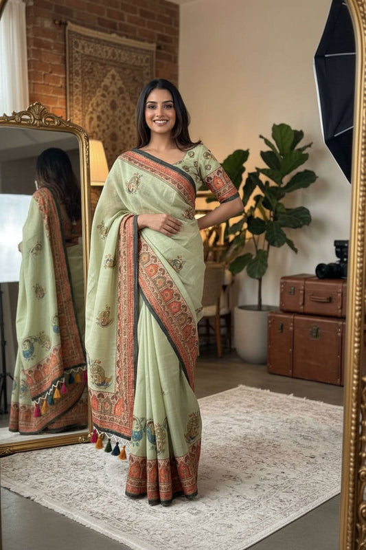 Woman in a light green saree with orange patterns taking a mirror selfie in a room.