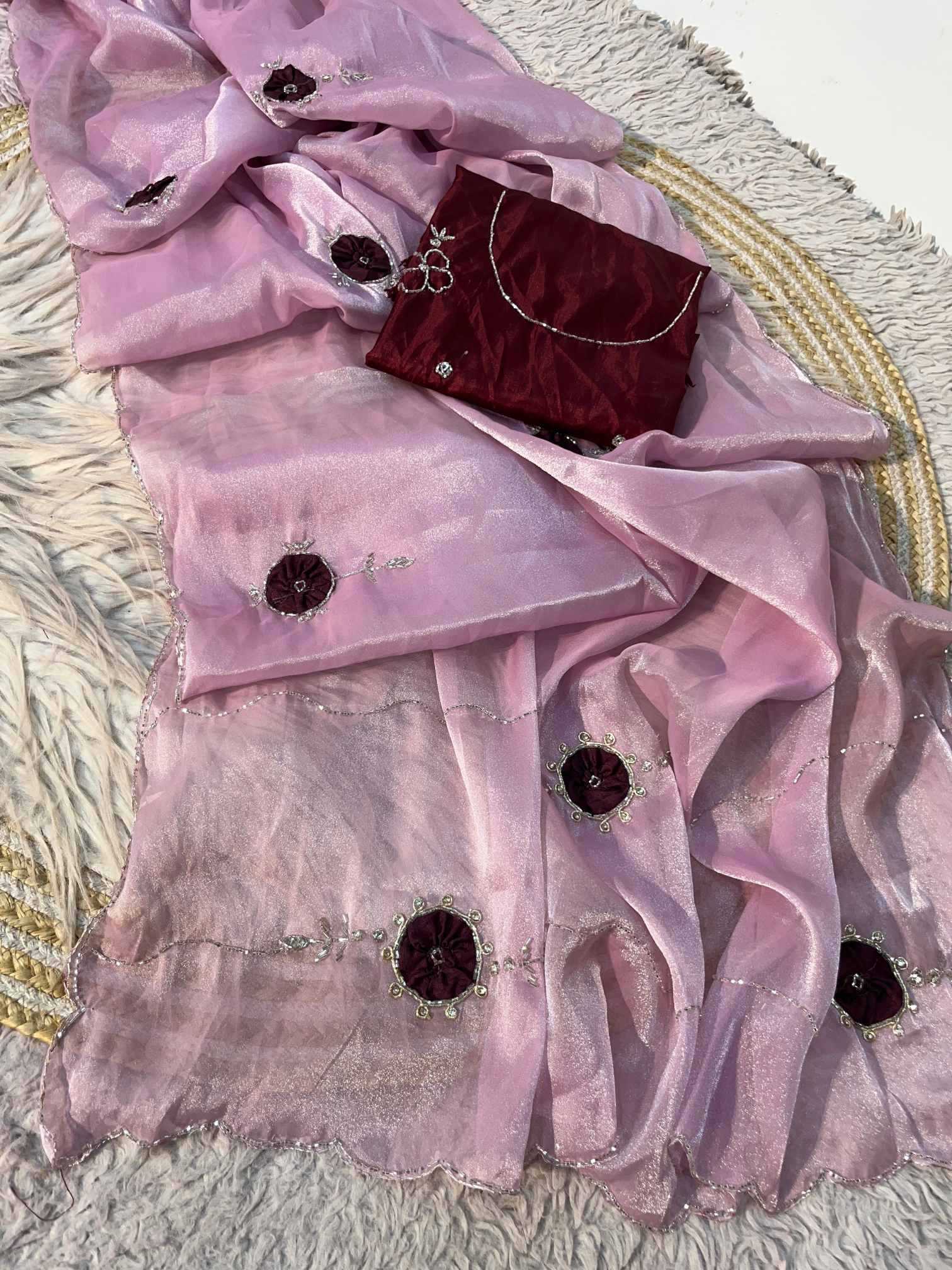 A light pink sheer organza dupatta with dark maroon embroidered floral motifs and silver mirror work, displayed alongside a matching dark maroon velvet clutch purse on a textured white rug.
