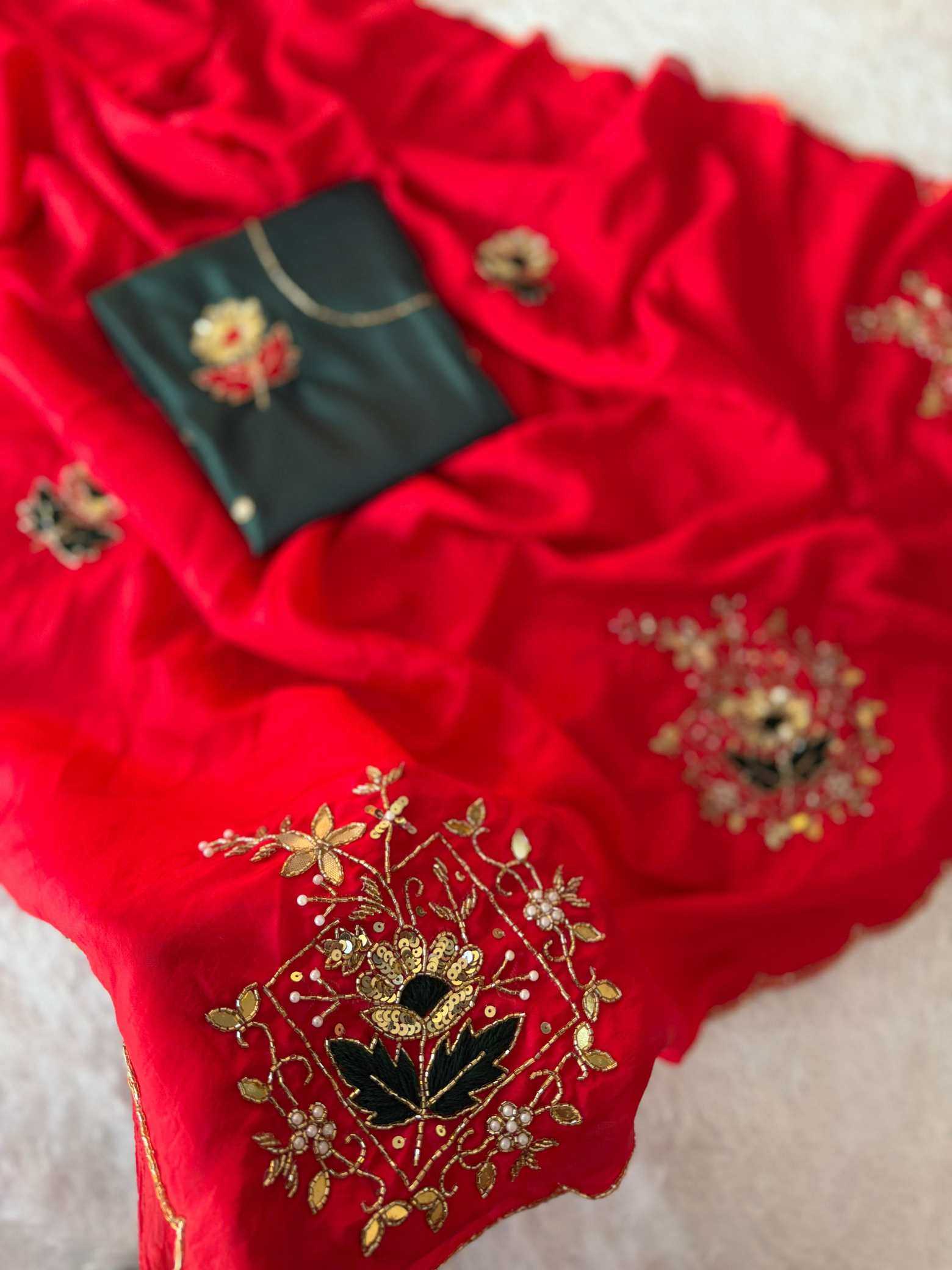 A bright red fabric garment or textile laid out on a light surface, decorated with gold floral embroidery and a small black embroidered pouch or accessory placed on top.
