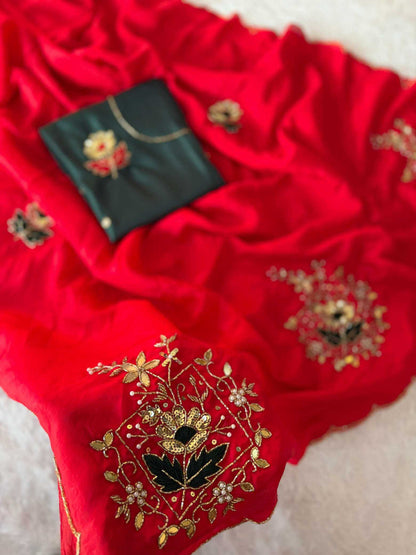 A bright red fabric garment or textile laid out on a light surface, decorated with gold floral embroidery and a small black embroidered pouch or accessory placed on top.