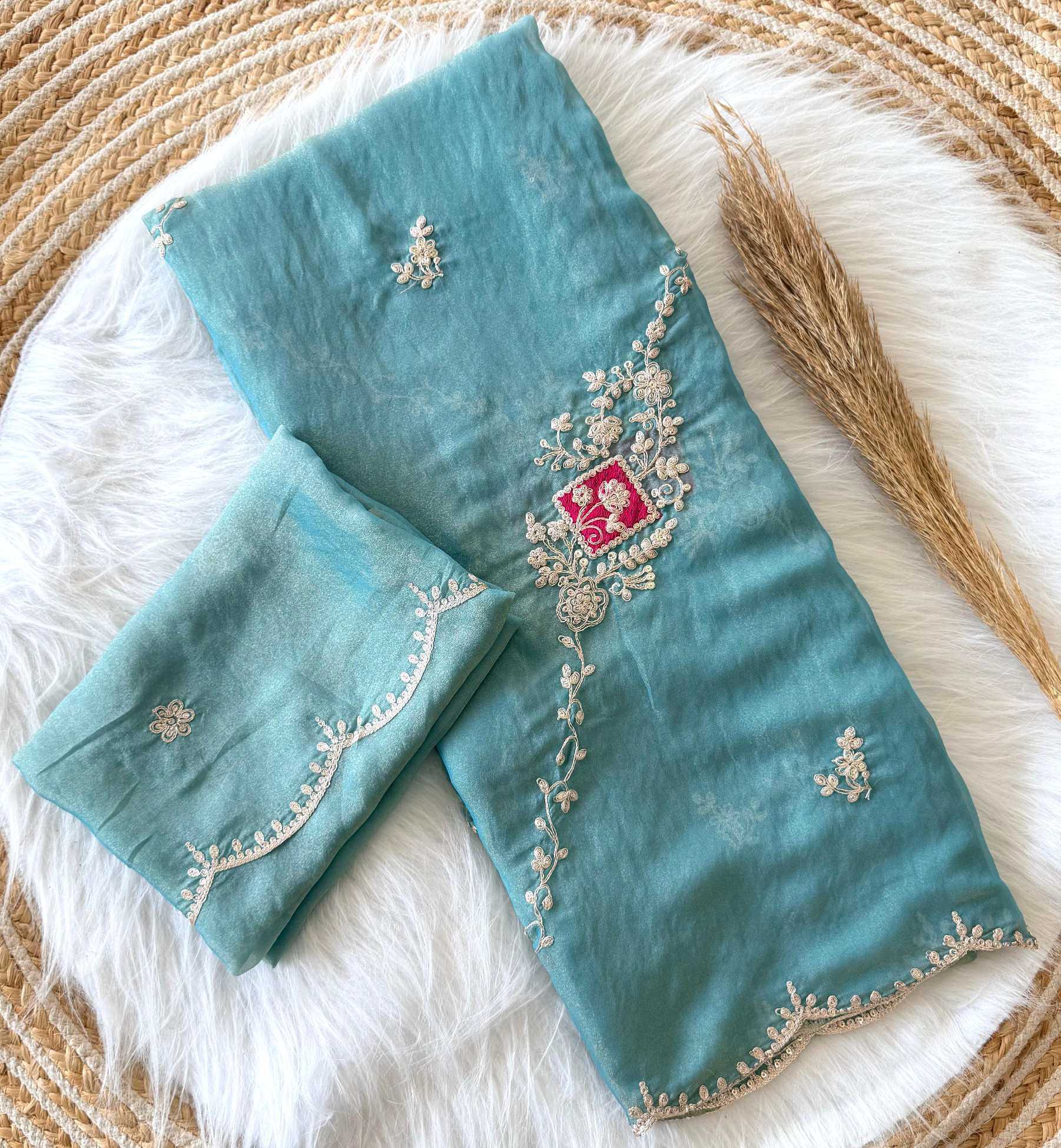 Teal fabric with intricate silver embroidery on a textured white and beige surface
