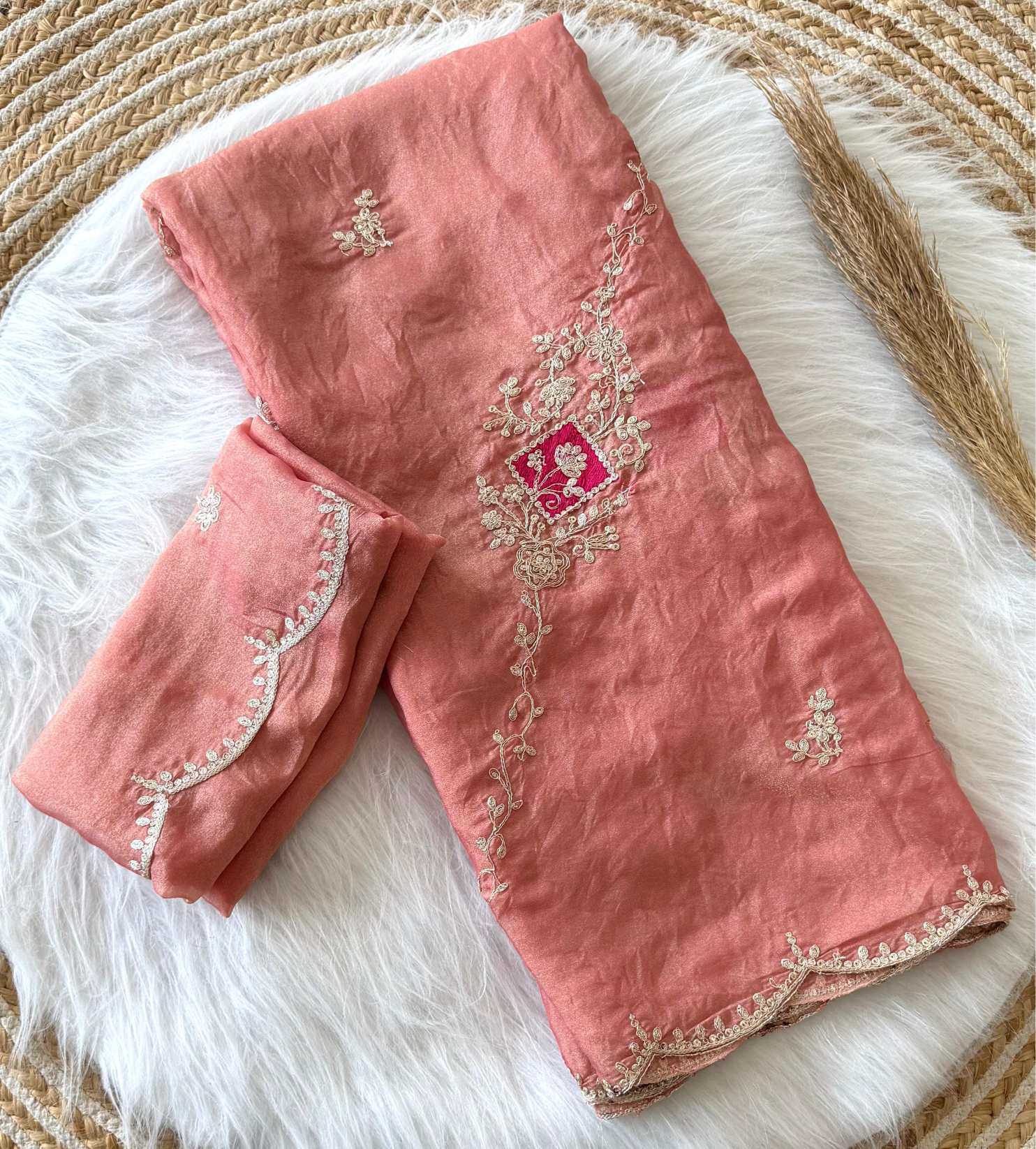A folded dusty pink traditional fabric set with intricate beige floral embroidery and a small pink and gold central motif, displayed on a white faux fur surface.