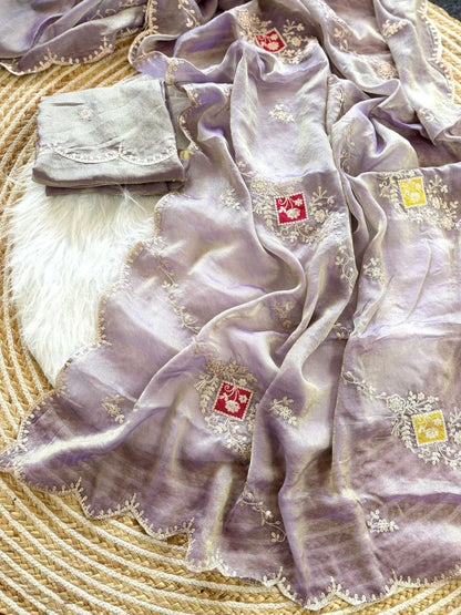 A lavender purple embroidered scarf with scalloped edges and small red and yellow embroidered squares, draped over a white faux fur rug on a woven straw mat.