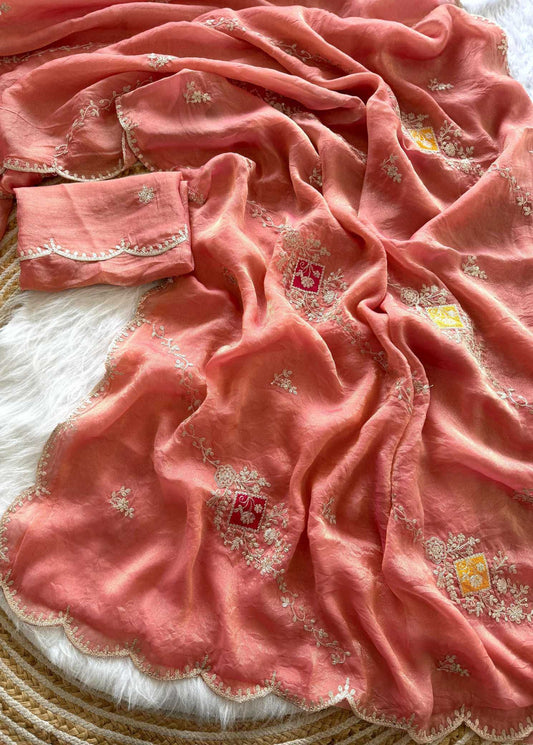 A peach-pink sheer fabric, likely a dupatta or scarf, draped over a white faux fur surface. The fabric features delicate white floral embroidery, small yellow accents, and scalloped edges.
