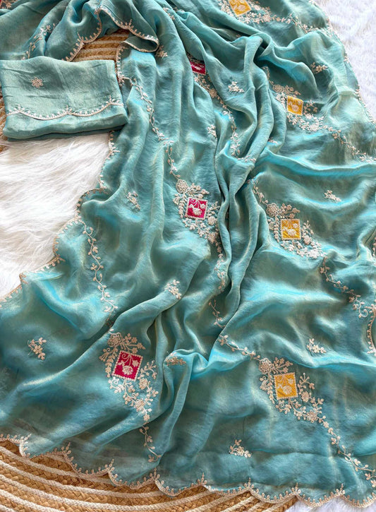 A turquoise blue dupatta with delicate white floral embroidery and small red and yellow embroidered motifs, draped elegantly on a woven mat.