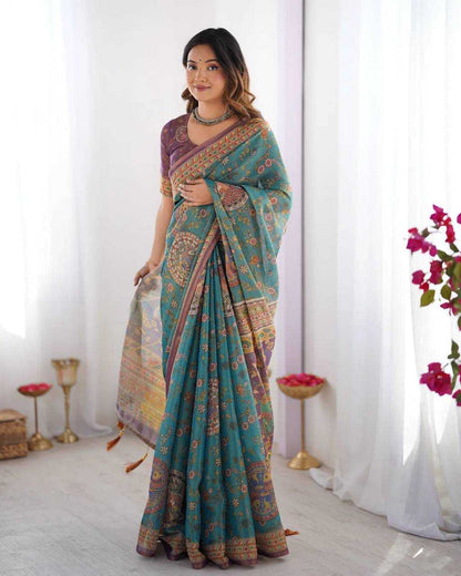 Woman wearing a teal saree with a colorful pattern in a bright room.
