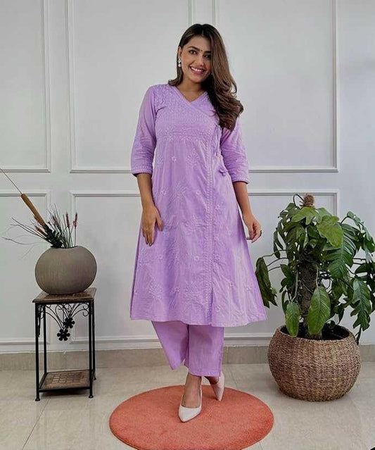 Woman in a purple outfit standing in a room with plants and a white wall.