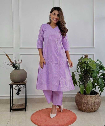 Woman in a purple outfit standing in a room with plants and a white wall.