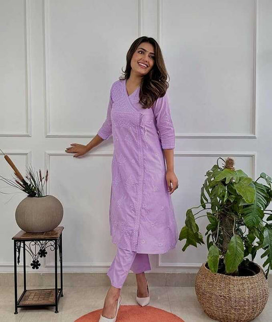 Woman in a purple outfit standing in a room with plants and a white wall.