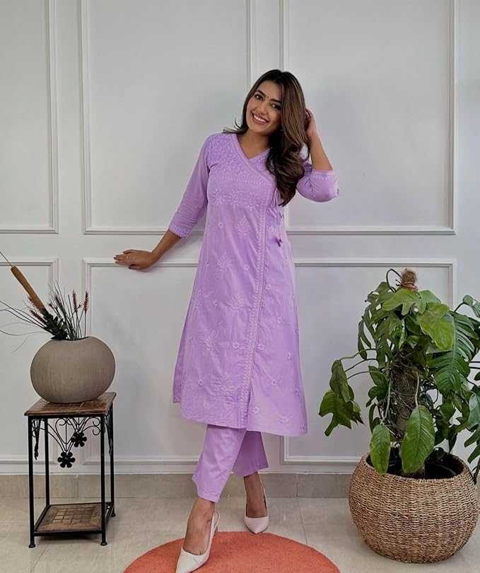 Woman in a purple outfit standing in a room with plants and a white wall.