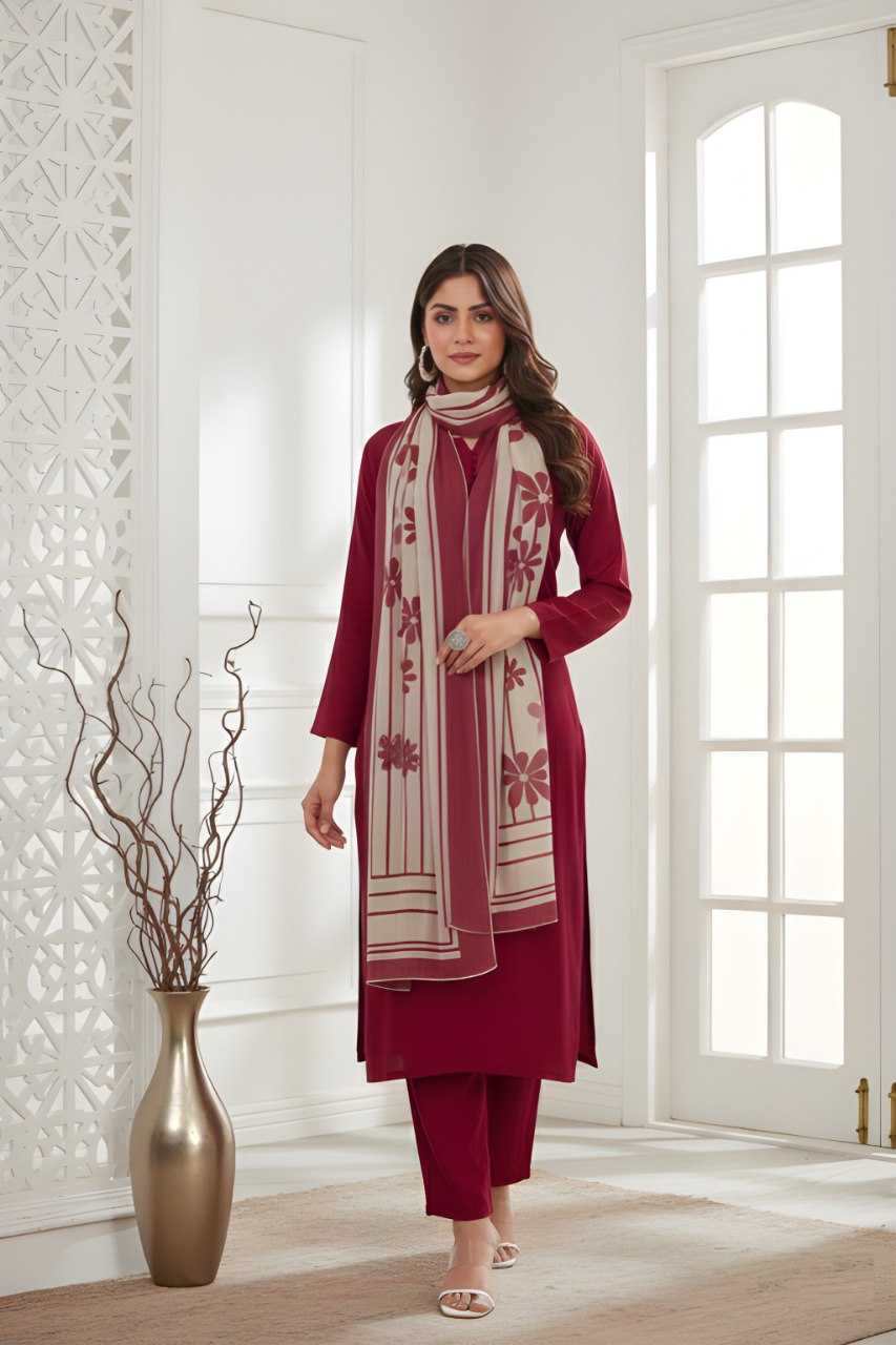 A woman models a three-piece maroon salwar kameez set with matching trousers and a cream dupatta featuring maroon floral embroidery, standing in a bright, modern white room.