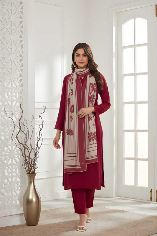 A woman models a three-piece maroon salwar kameez set with matching trousers and a cream dupatta featuring maroon floral embroidery, standing in a bright, modern white room.