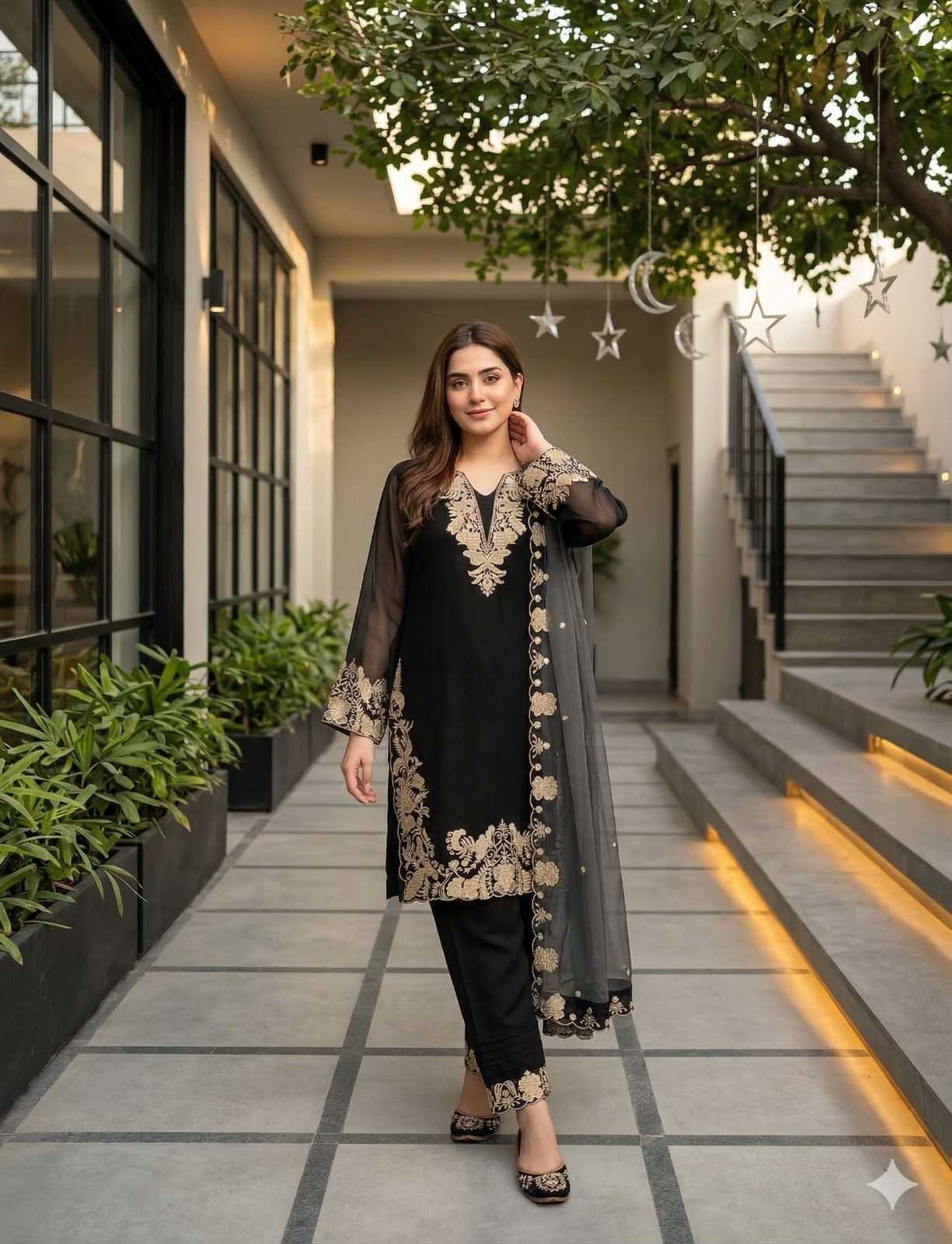 Woman in black and gray traditional outfit standing in a modern outdoor setting with plants and stairs.