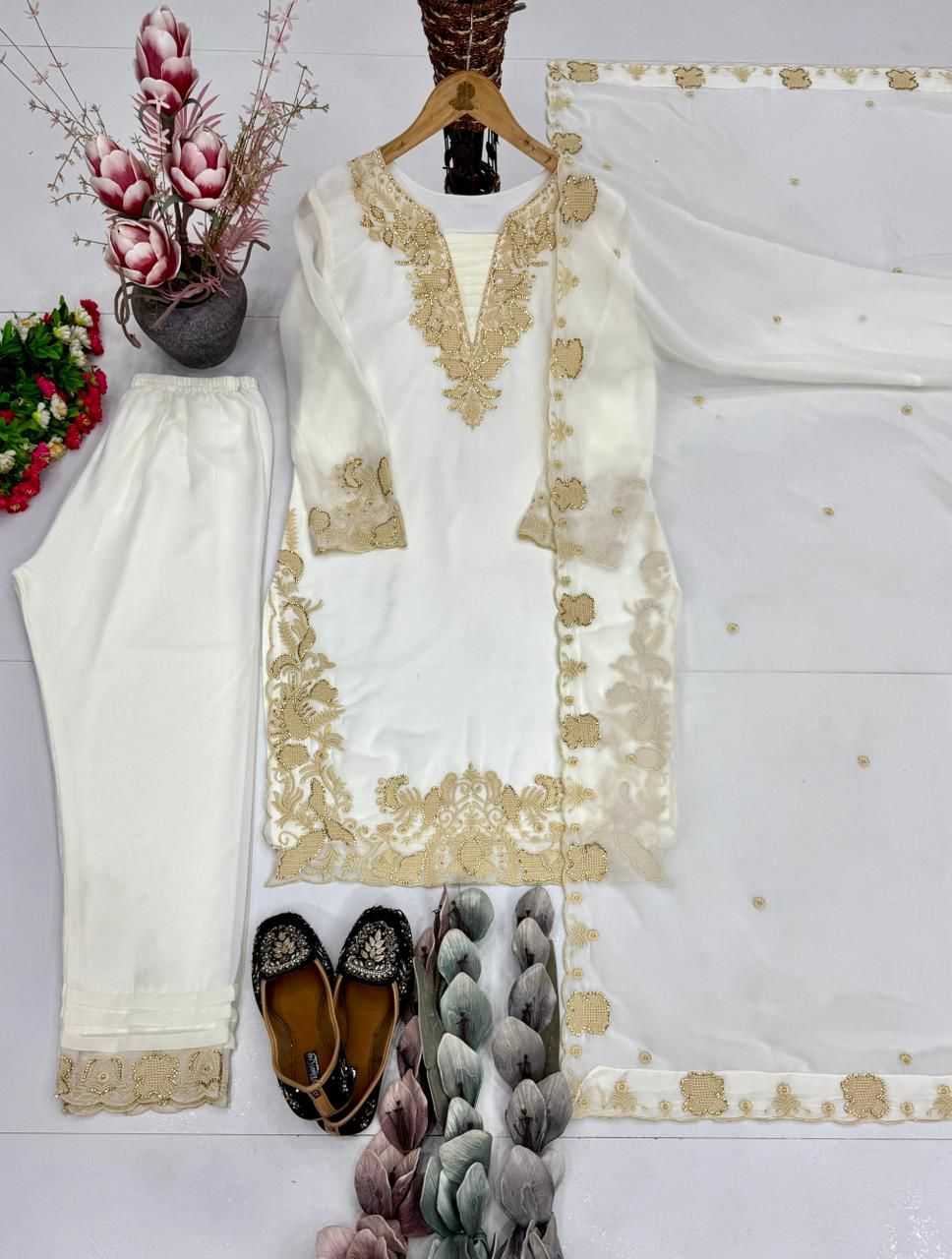 White embroidered outfit with gold details, shoes, and a decorative plant on a white background