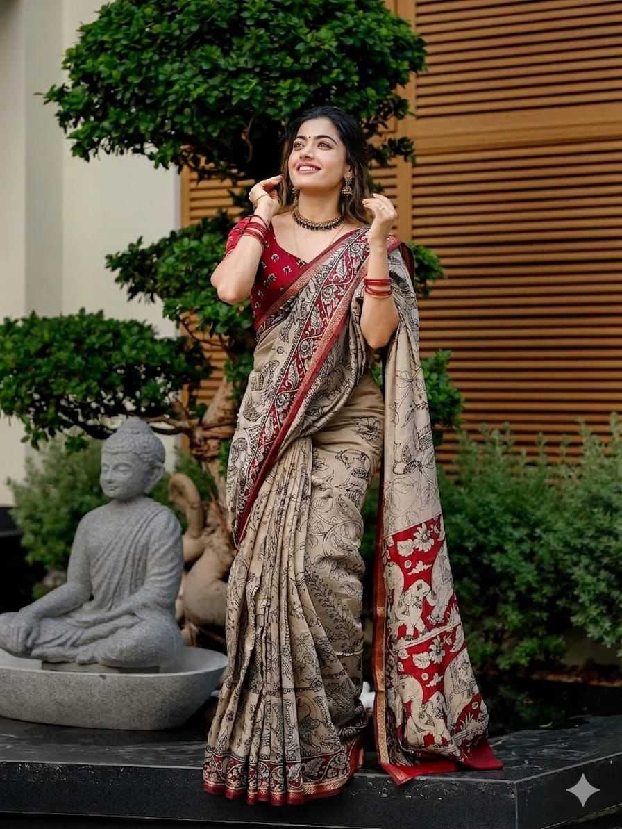 Woman in a saree standing outdoors with greenery and a statue in the background