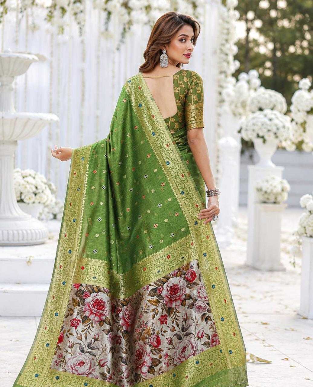 Woman wearing a green saree with floral patterns in an outdoor setting with white flowers.
