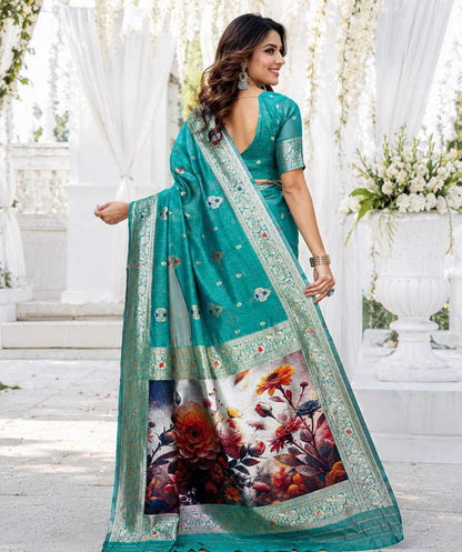 Woman wearing a teal saree with floral patterns in an outdoor setting.