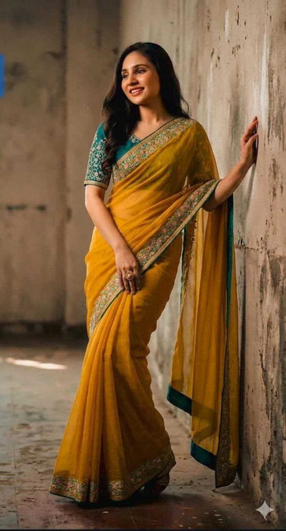 Woman in a yellow saree with green and gold details against a textured wall.