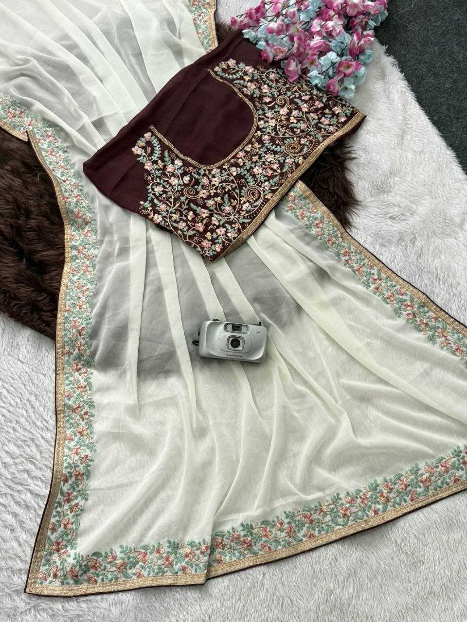 White saree with floral border and embroidered blouse on a textured surface.